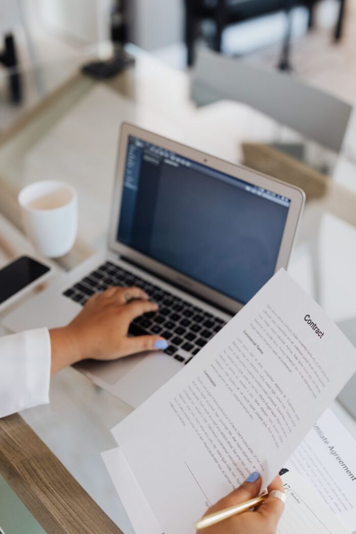 person holding a document while using laptop